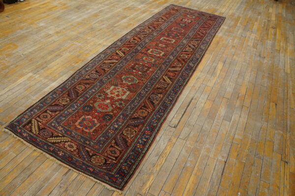 Red and blue patterned runner rug with geometric designs is displayed on light, distressed wood plank flooring.