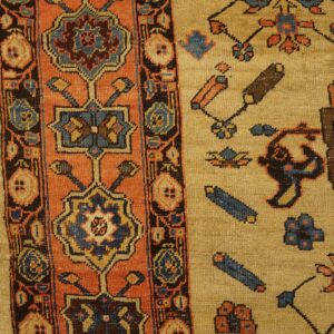 Tan rug with rust and dark blue geometric patterns resting on distressed pale wood flooring.