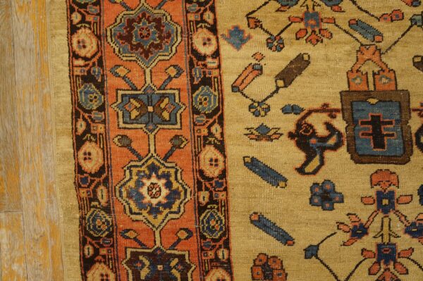 Tan rug with rust and dark blue geometric patterns resting on distressed pale wood flooring.