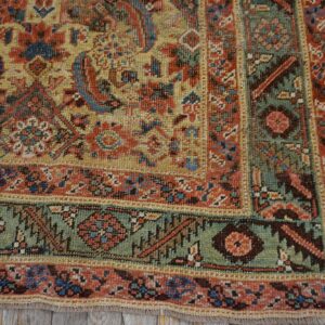 Low-pile rug corner showing detailed red, yellow, and green borders over rustic gray wood planks.