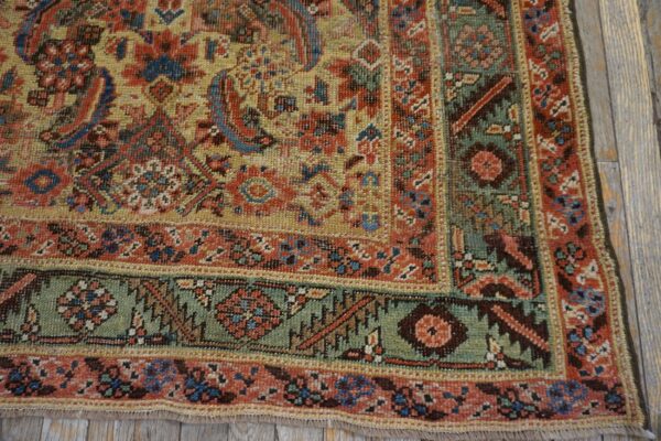 Low-pile rug corner showing detailed red, yellow, and green borders over rustic gray wood planks.