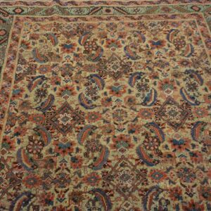 Muted gold rug with complex red and blue floral patterns rests on weathered gray plank flooring.