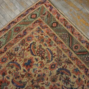 Close-up of a rug corner featuring red, gold, blue, and green geometric patterns on distressed gray wood flooring.