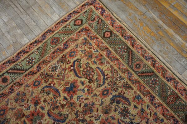 Close-up of a rug corner featuring red, gold, blue, and green geometric patterns on distressed gray wood flooring.