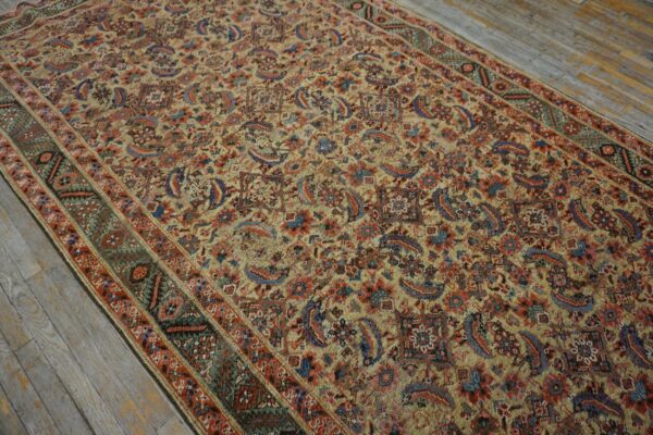 Ornate low-pile area rug in beige, red, and blue floral motifs rests on distressed gray wooden floorboards.