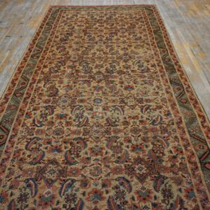 A long runner rug featuring a dense tan, red, and blue traditional pattern on worn wood flooring.