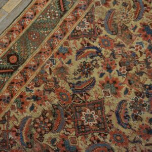 Intricate traditional rug pattern in muted gold, blue, and red with a detailed border on weathered planks.
