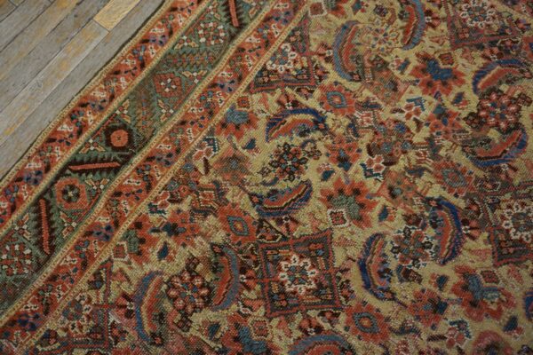 Intricate traditional rug pattern in muted gold, blue, and red with a detailed border on weathered planks.