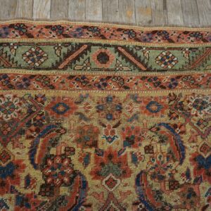 Detail shot of a muted traditional rug featuring red, blue, green, and gold colors near distressed wood.