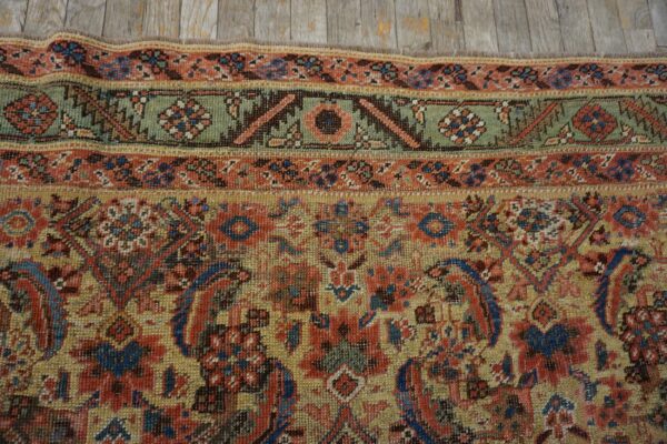 Detail shot of a muted traditional rug featuring red, blue, green, and gold colors near distressed wood.