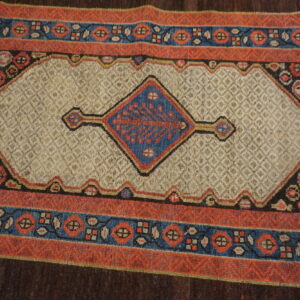 A textured rug with a central blue diamond medallion on a beige field and geometric red-orange borders.