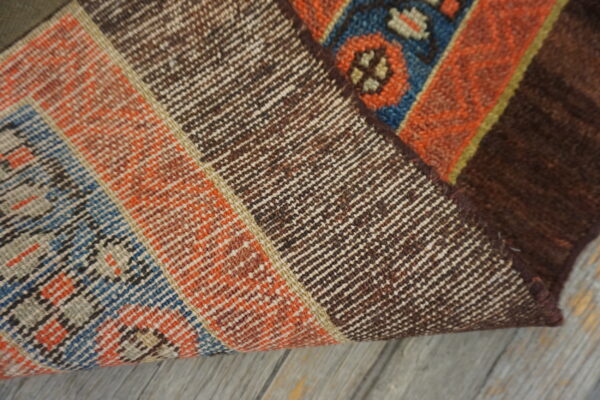 Rug corner folded back exposing the tight brown weave backing next to the low-pile orange and blue pattern.