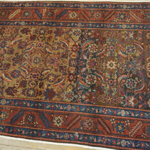 Traditional low-pile rug with geometric and floral patterns in red, khaki, and blue, visible on wood planks.