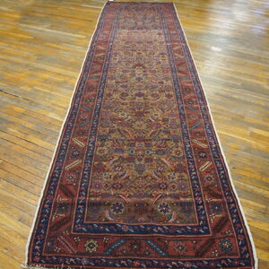 Red, blue, and gold patterned runner rug displayed lengthwise on distressed, wide-plank wooden flooring.