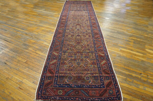 Red, blue, and gold patterned runner rug displayed lengthwise on distressed, wide-plank wooden flooring.