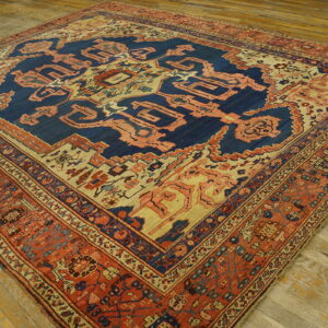 Ornate patterned rug in blue, peach, and terracotta colors laid diagonally on distressed wood flooring.