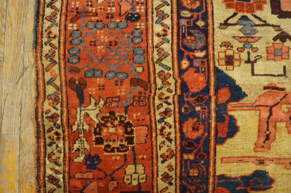 Close-up of a rug with deep red, navy blue, and khaki traditional geometric patterns next to wood flooring.