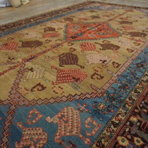 Tan field rug with stylized rust, blue, and brown animal patterns on exposed wood flooring.