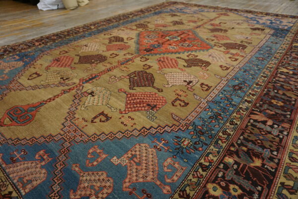 Tan field rug with stylized rust, blue, and brown animal patterns on exposed wood flooring.