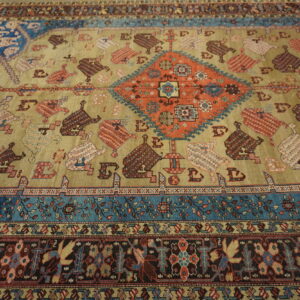 Tan field rug with a rust central diamond, blue accents, and repeating stylized tribal motifs.