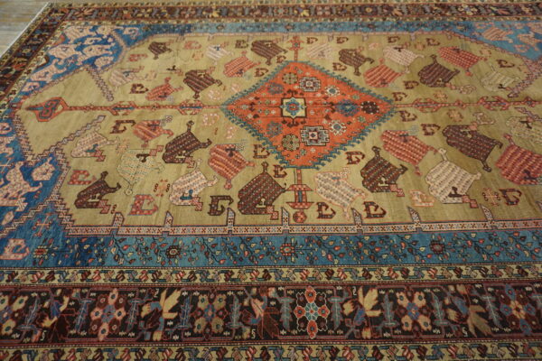 Tan field rug with a rust central diamond, blue accents, and repeating stylized tribal motifs.