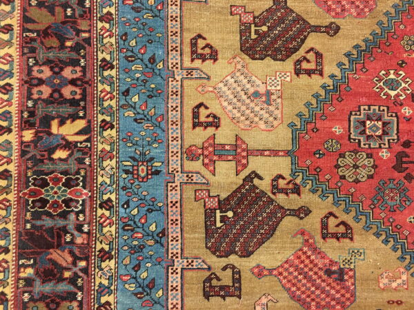 Geometric rug pattern featuring golden tan, deep red, and turquoise designs with stylized animal figures and stepped borders.
