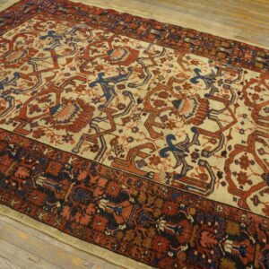 Area rug with beige field, rust red and blue stylized designs, and dark borders on light wood plank flooring.