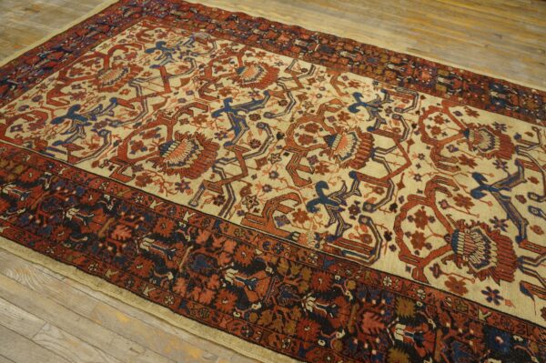 Area rug with beige field, rust red and blue stylized designs, and dark borders on light wood plank flooring.