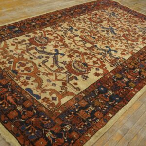 Low pile rug with an ivory field, rust and navy stylized patterns, bordered in dark blue on wooden flooring.