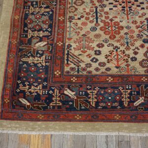 Low-pile rug with a beige field and detailed red and navy borders lies on distressed wood floors.