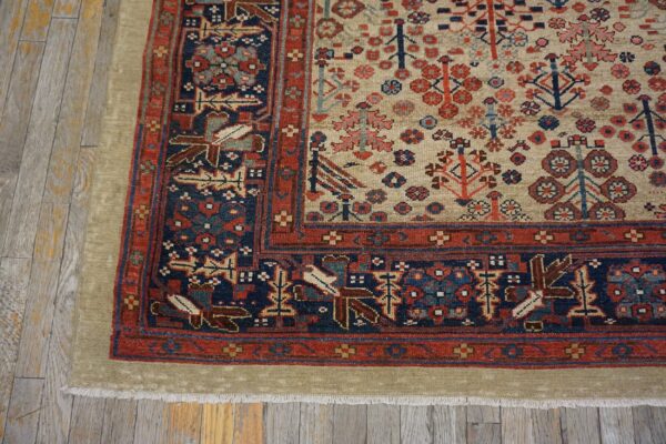 Low-pile rug with a beige field and detailed red and navy borders lies on distressed wood floors.
