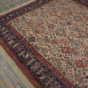 Beige rug with red and navy patterned field and borders rests on weathered gray wood planks.