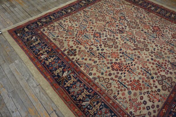 Beige rug with red and navy patterned field and borders rests on weathered gray wood planks.