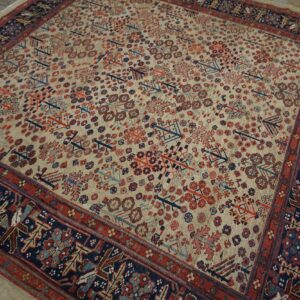 Beige rug with repeating red and blue geometric motifs and wide navy borders on a wood floor.