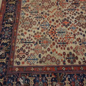 Geometric patterned rug with a tan field and red, navy, and blue motifs resting on weathered wooden flooring.