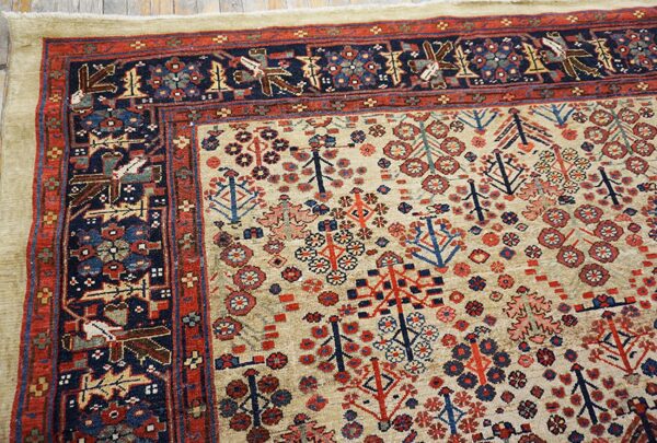 Beige rug field featuring dense red and blue stylized tree motifs framed by a navy geometric animal border.