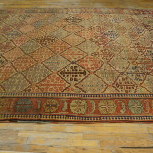 Muted red, beige, and blue rug with a dense geometric diamond pattern laid upon light wood planks.
