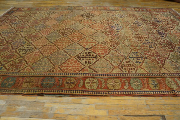 Muted red, beige, and blue rug with a dense geometric diamond pattern laid upon light wood planks.