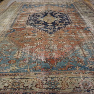 Distressed rug with a geometric pattern in terracotta, navy, and teal laid upon wooden plank flooring.
