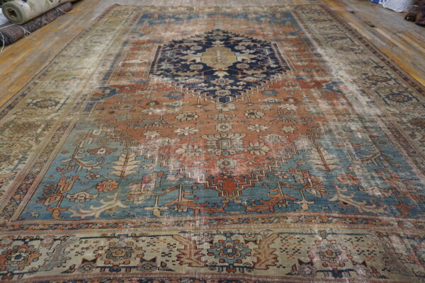 Distressed rug with a geometric pattern in terracotta, navy, and teal laid upon wooden plank flooring.