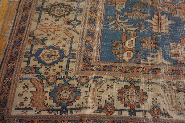 Distressed traditional rug corner showing blue, beige, and orange motifs next to yellow wood floor.