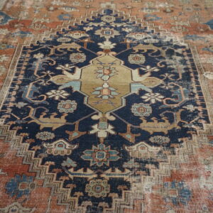 A highly distressed traditional rug features a navy field, terracotta border, and tan central medallion.