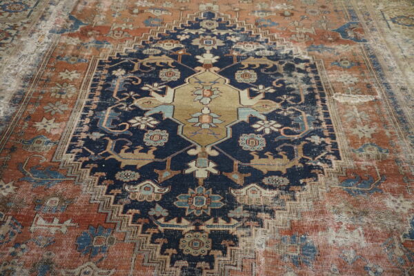 A highly distressed traditional rug features a navy field, terracotta border, and tan central medallion.