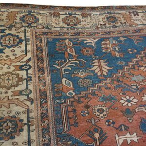 The corner of a low pile rug featuring stylized motifs in blue, terracotta, and cream colors.