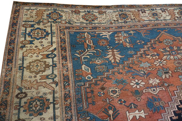 The corner of a low pile rug featuring stylized motifs in blue, terracotta, and cream colors.