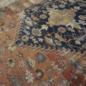 Close-up of a faded traditional rug featuring navy and rust fields separated by geometric chevron borders.