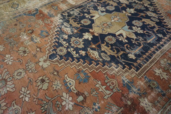 Close-up of a faded traditional rug featuring navy and rust fields separated by geometric chevron borders.
