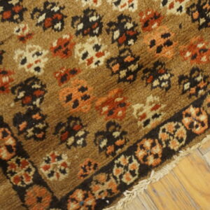 High-pile brown rug featuring scattered rust, black, and cream patterns with a dark border on wood flooring.