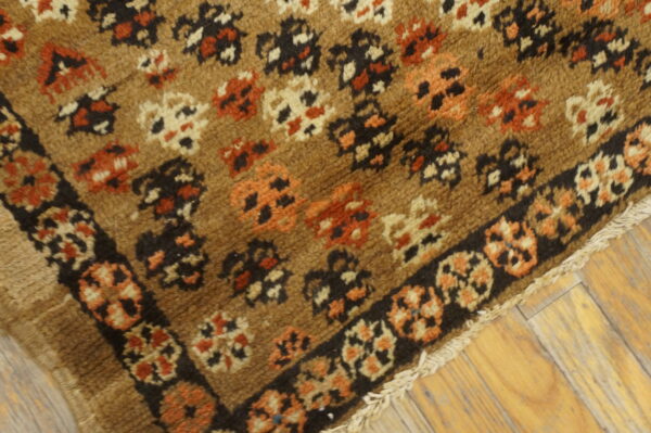 High-pile brown rug featuring scattered rust, black, and cream patterns with a dark border on wood flooring.