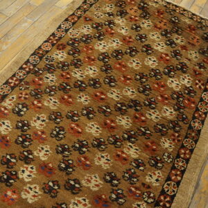 A tan rug with dense stylized patterns in black, red, and cream on distressed wood floors.